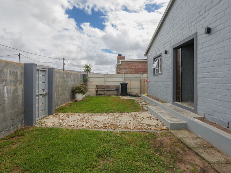A private rear garden featuring a lawn, stone pathway, and concrete boundary walls, providing a functional outdoor space adjacent to the main dwelling.