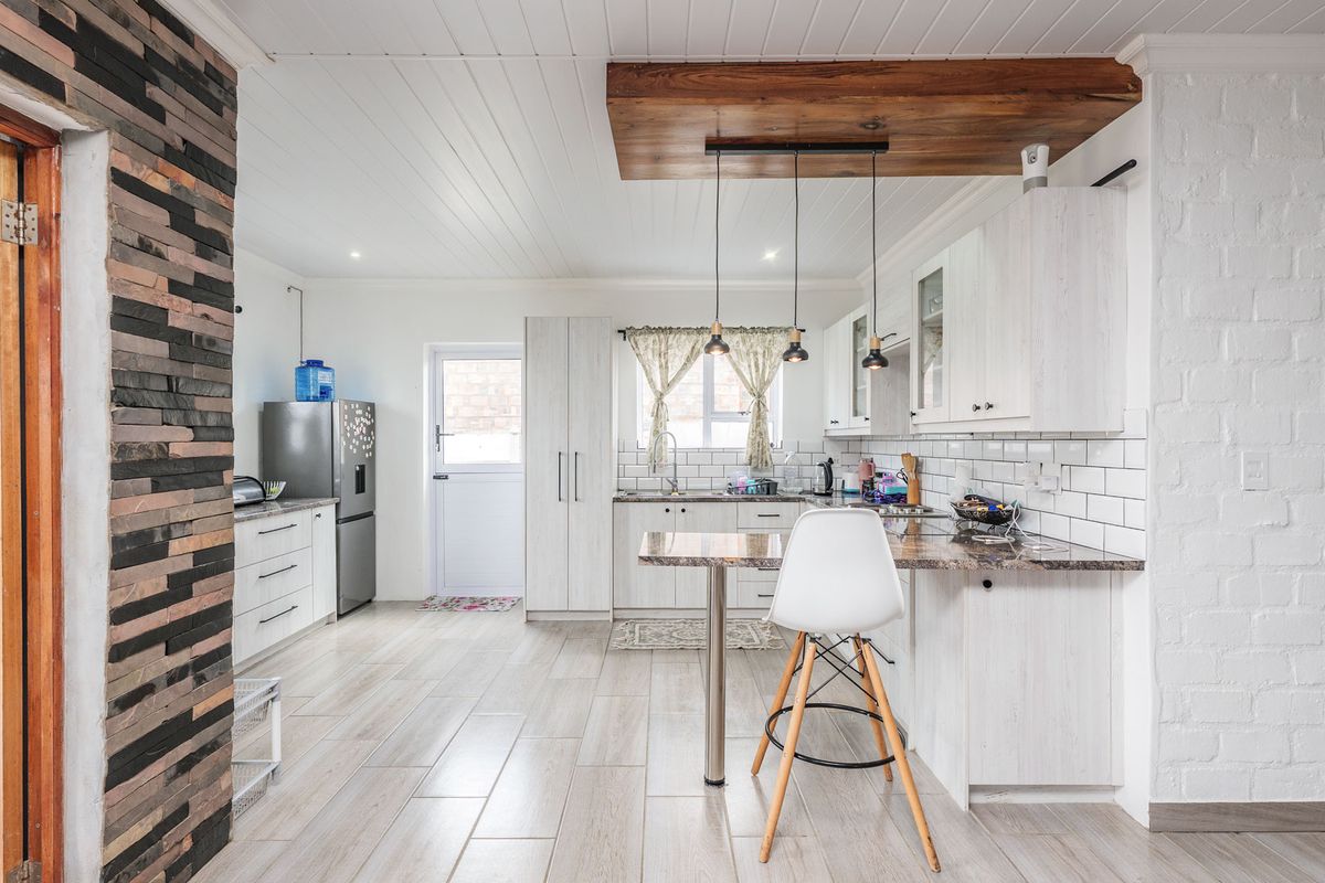 Modern kitchen featuring white cabinetry, subway tile backsplash, stone countertops, a breakfast bar, and a unique timber ceiling feature with pendant lighting.
