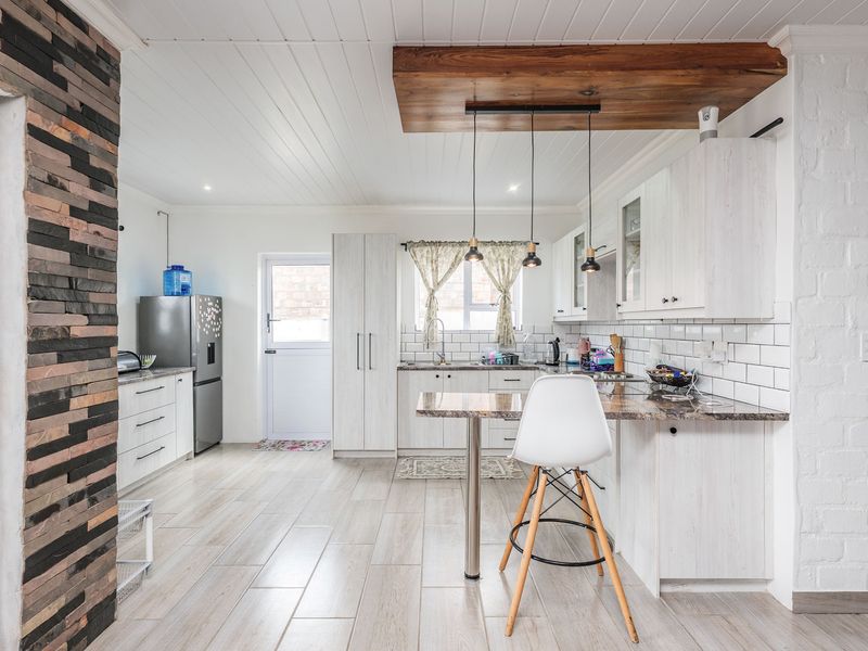 Modern kitchen featuring white cabinetry, subway tile backsplash, stone countertops, a breakfast bar, and a unique timber ceiling feature with pendant lighting.