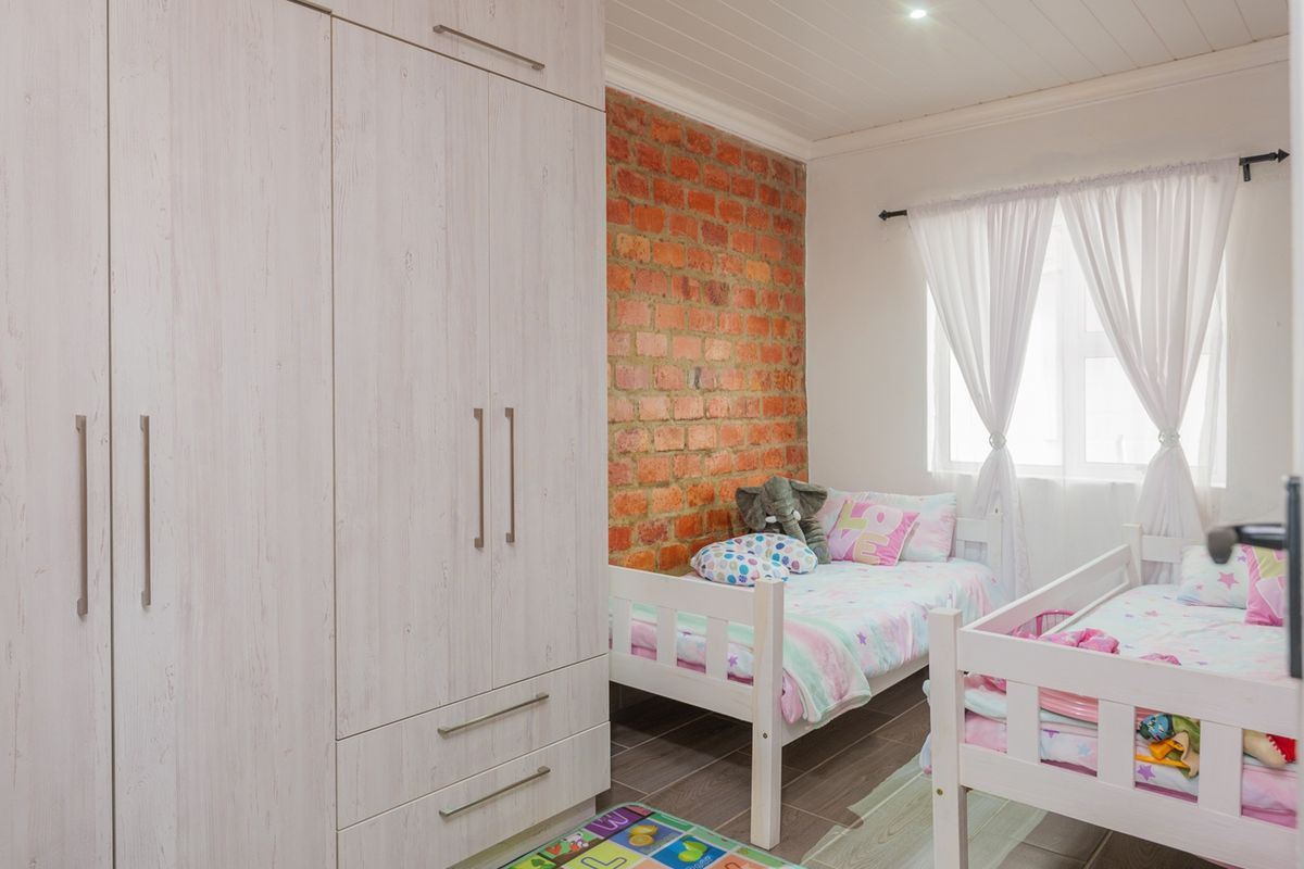 A well-maintained bedroom featuring a large built-in wardrobe, an exposed brick feature wall, tiled flooring, and a classic tongue and groove ceiling.