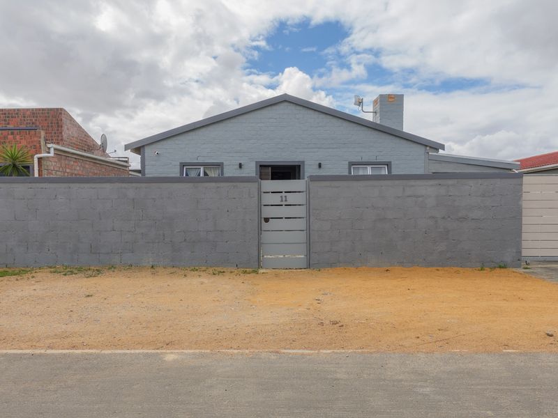 Front elevation of a single-story house featuring a painted brick facade, perimeter wall, and gated entrance with a driveway.