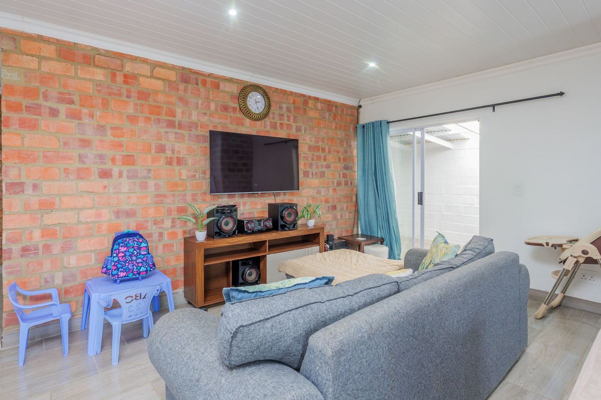 A comfortable living room featuring an exposed brick wall, tiled flooring, and direct access to an outdoor area through sliding glass doors.