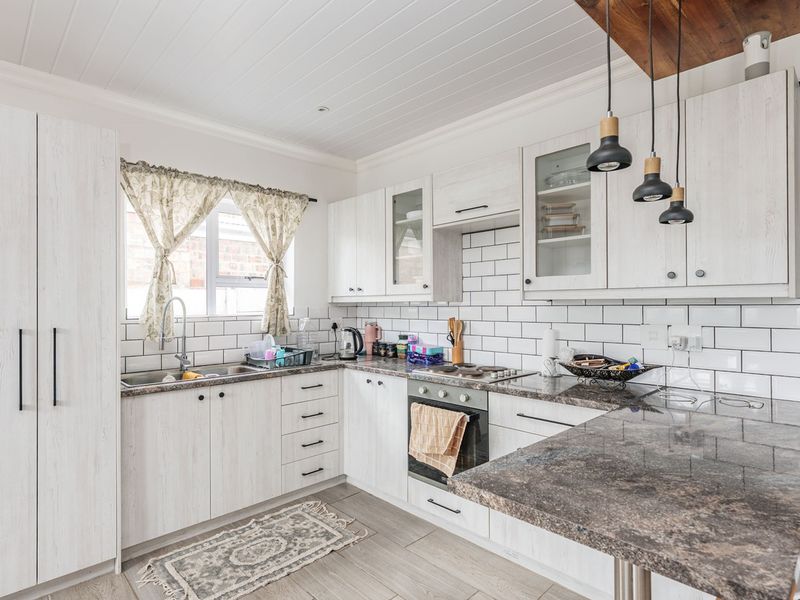 A well-maintained kitchen featuring light wood-grain cabinetry, granite countertops, subway tile backsplash, and modern pendant lighting.