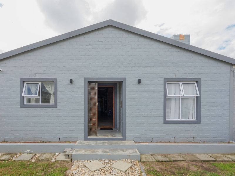 Front elevation of a single-story house featuring a painted brick facade, central entrance with security gate, and attached garage.