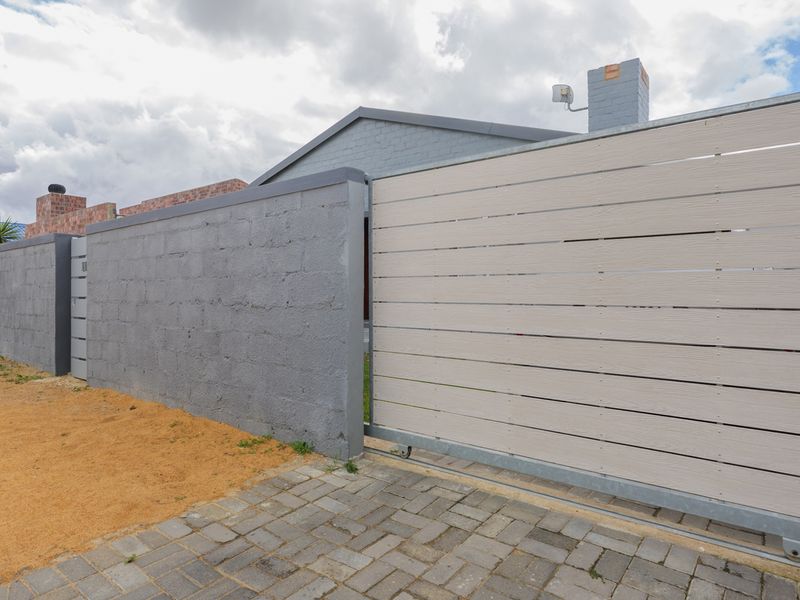 A view of the property's front boundary featuring a modern horizontal slat sliding gate and a painted masonry wall with a paved driveway.