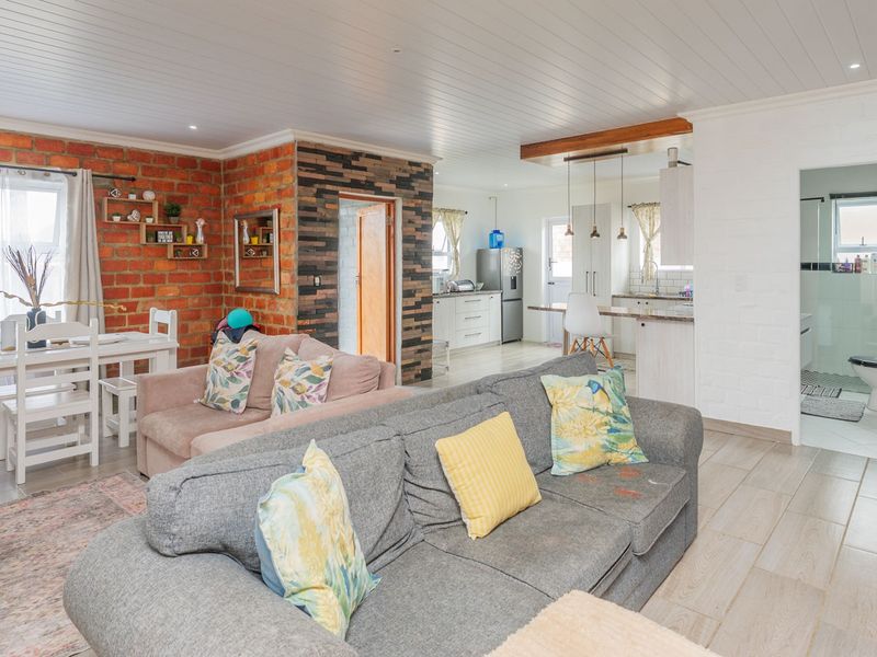 Spacious open-plan living and dining area featuring exposed brick walls, timber-look tile flooring, and a modern kitchen with integrated cabinetry and pendant lighting.