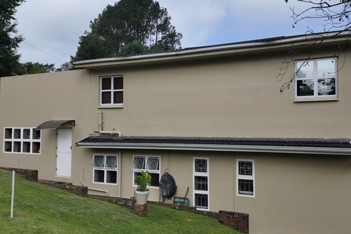 A view of the rear exterior elevation of the house, featuring a multi-level facade with white-framed windows and a sloped lawn area.