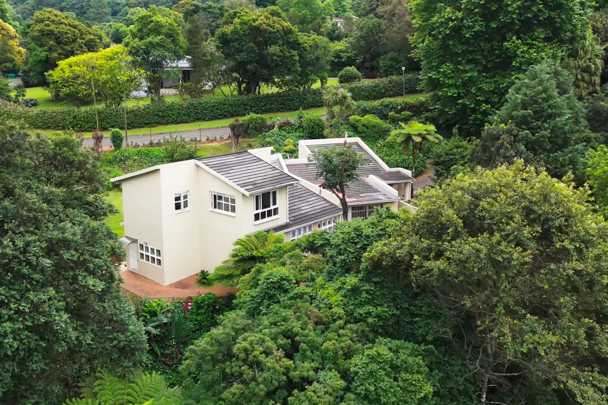 An elevated aerial view of a multi-level residential property nestled within a lush, mature garden setting with extensive surrounding greenery.