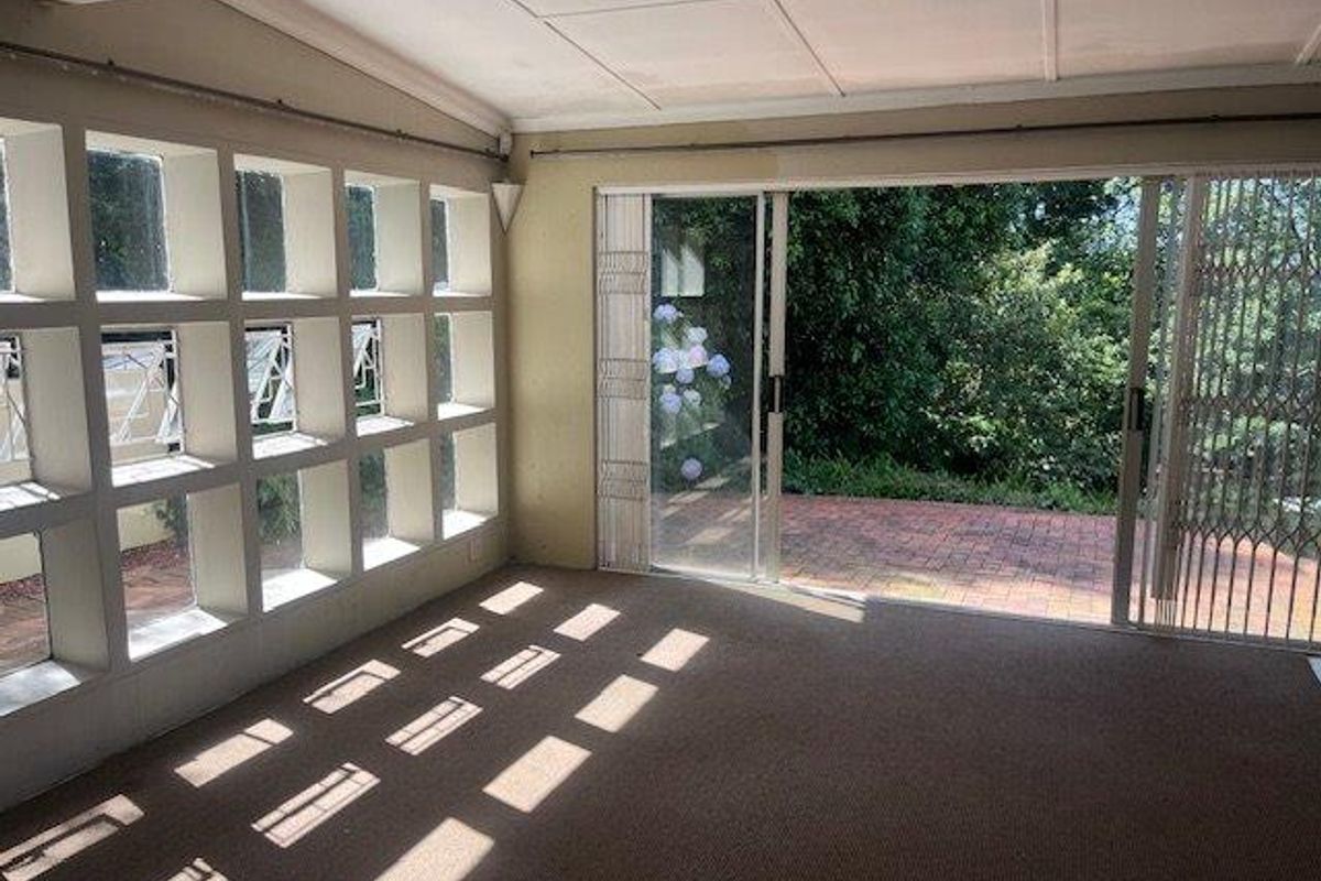 A sunlit living room featuring a large grid-style window wall and sliding glass doors that open onto a paved outdoor patio area.