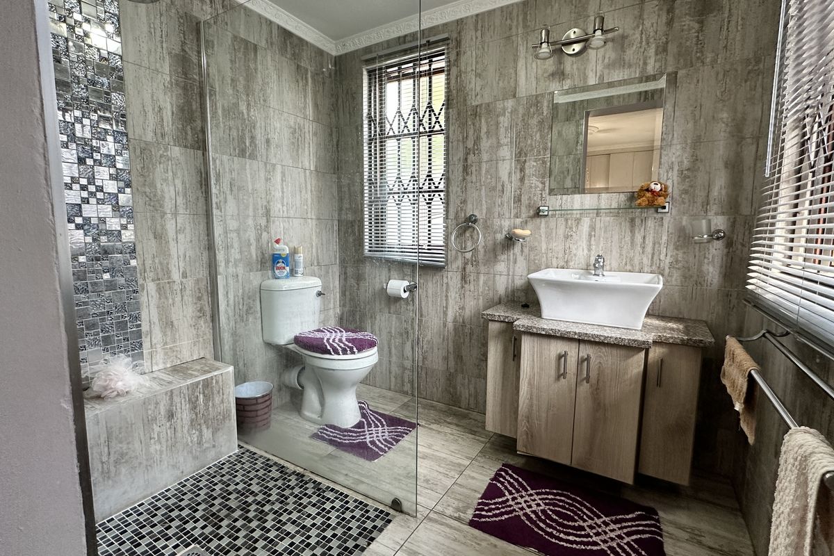 Modern bathroom featuring floor-to-ceiling textured tiling, a glass-enclosed walk-in shower, a vessel sink vanity, and a window with security bars.