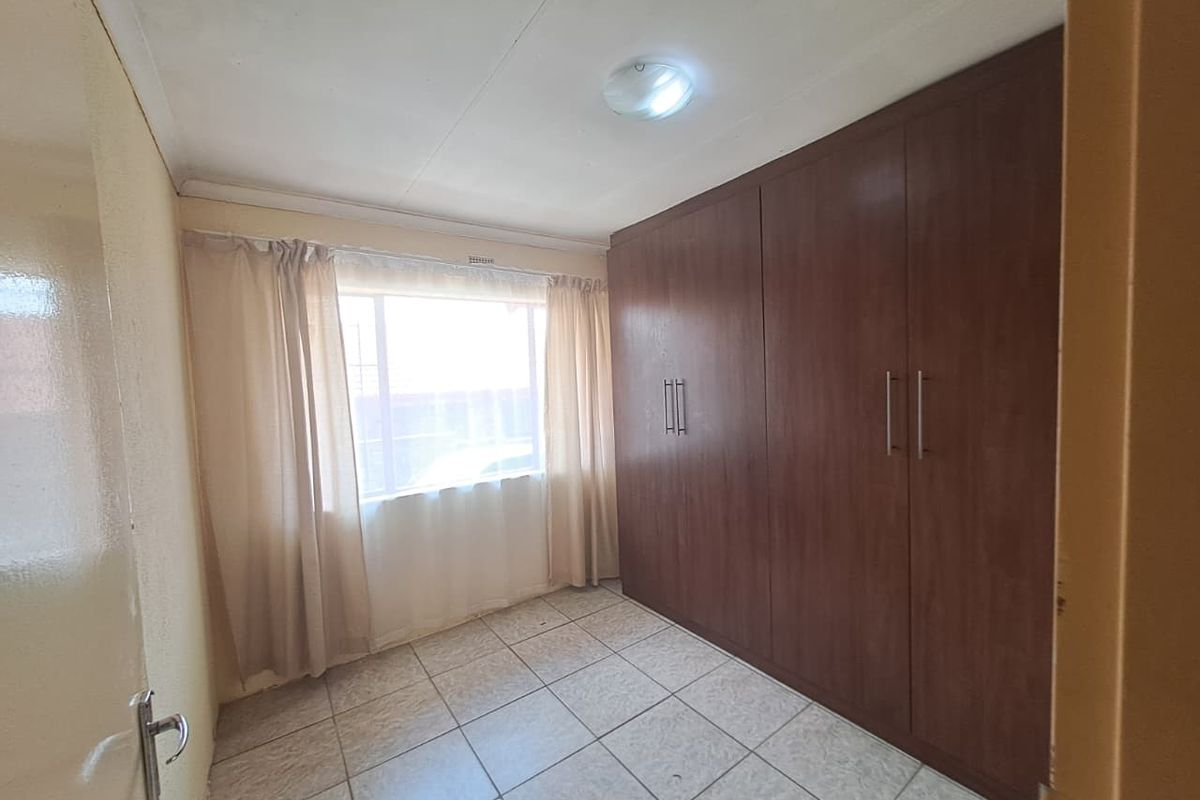 A clean, empty bedroom featuring tiled flooring and extensive built-in wooden cupboards, offering ample storage space.