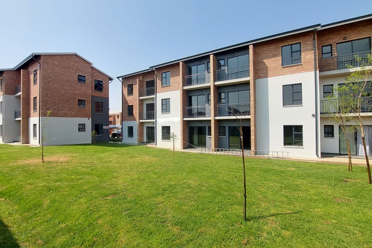 Exterior view of a modern apartment complex featuring brick and rendered facades, private balconies, and a well-maintained communal lawn area.