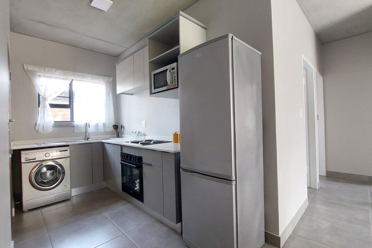 Modern kitchen featuring grey cabinetry, built-in oven, hob, extractor fan, and integrated space for a washing machine with tiled flooring.