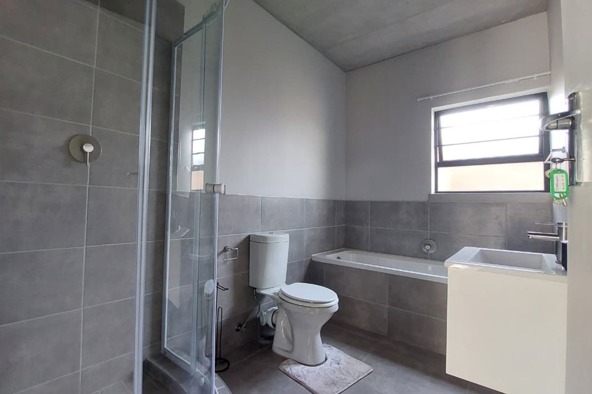 Modern bathroom featuring a glass-enclosed shower, a built-in bathtub, a wall-mounted vanity, and neutral grey floor-to-ceiling tiling.