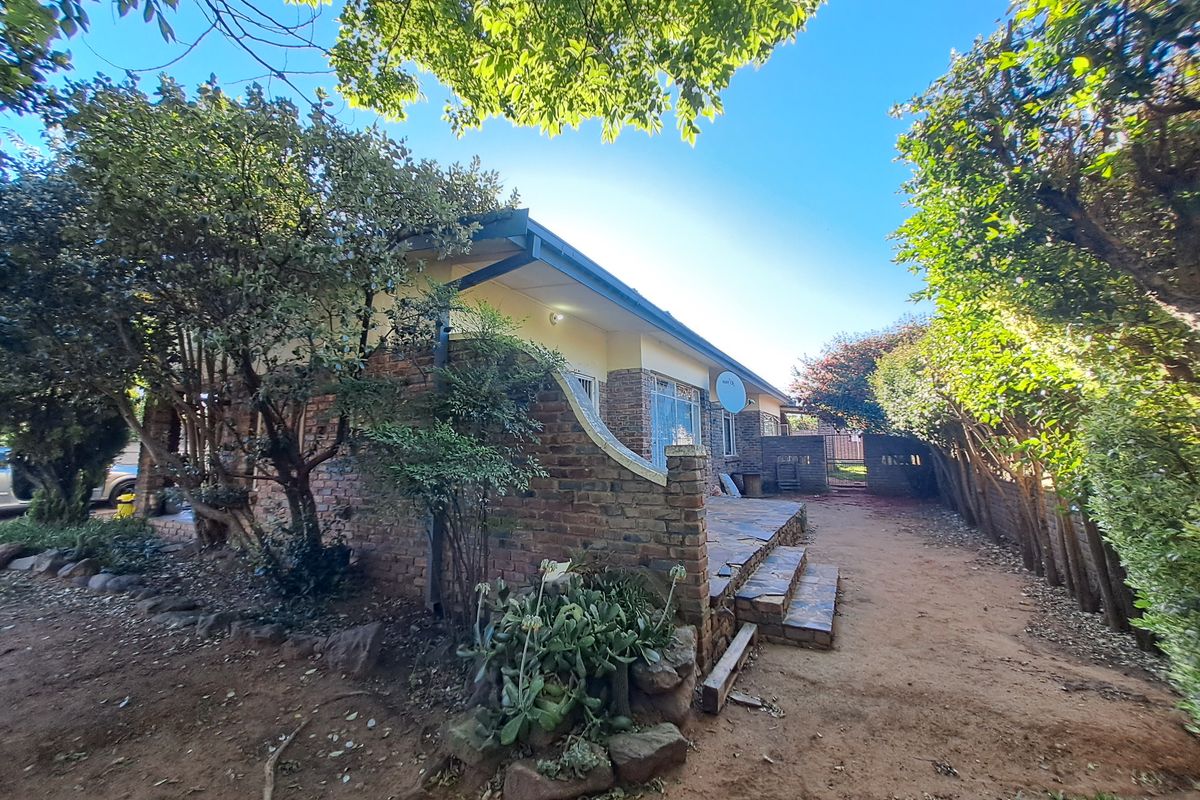 Rear view of the property featuring a brick facade, a tiled patio area, and established garden surroundings.