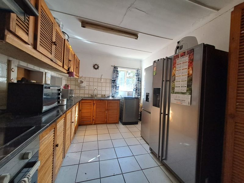 A functional kitchen featuring wooden cabinetry, tiled flooring, and a tiled backsplash, offering a dated aesthetic with potential for modernization.