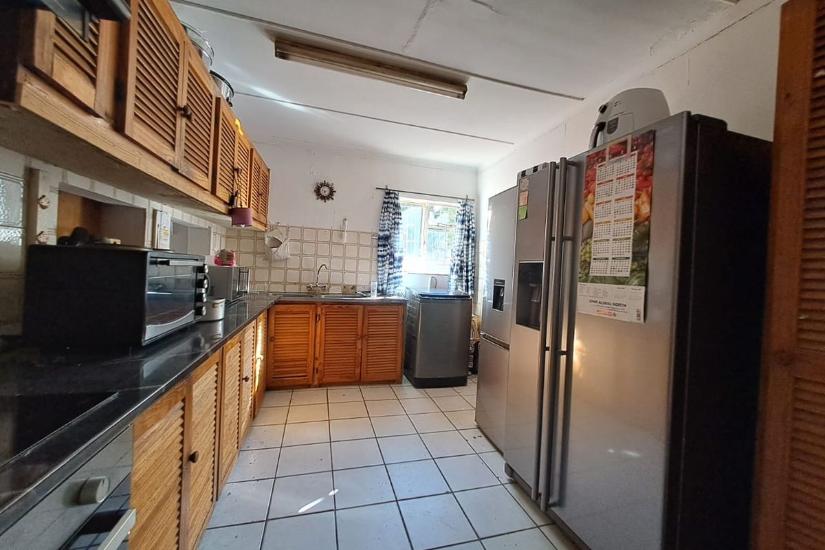 A functional kitchen featuring wooden cabinetry, tiled flooring, and a tiled backsplash, offering a dated aesthetic with potential for modernization.