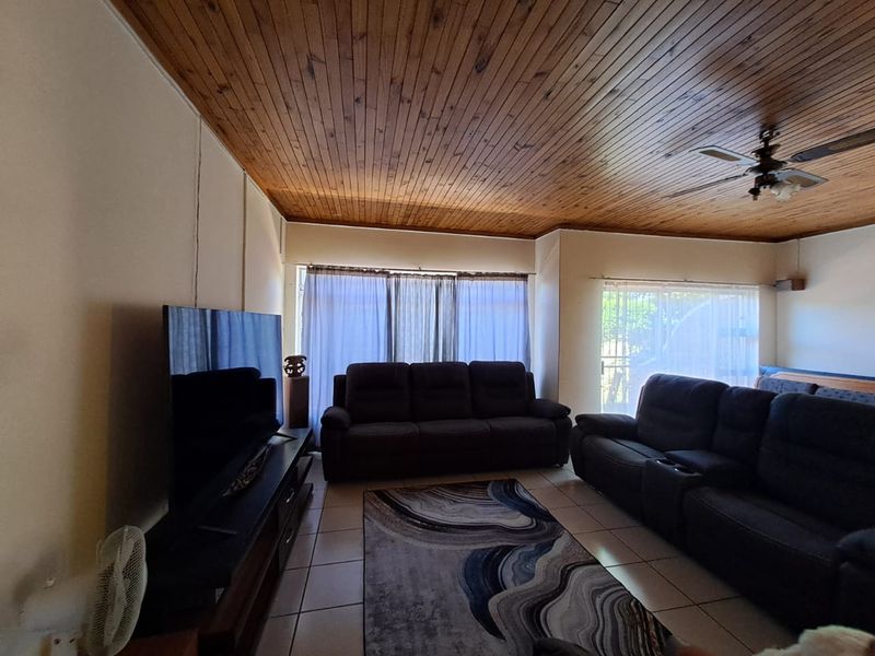 A living room featuring a timber tongue and groove ceiling, ceiling fan, and tiled flooring, providing a functional and comfortable space.