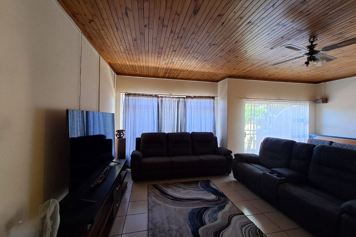 A living room featuring a timber tongue and groove ceiling, ceiling fan, and tiled flooring, providing a functional and comfortable space.