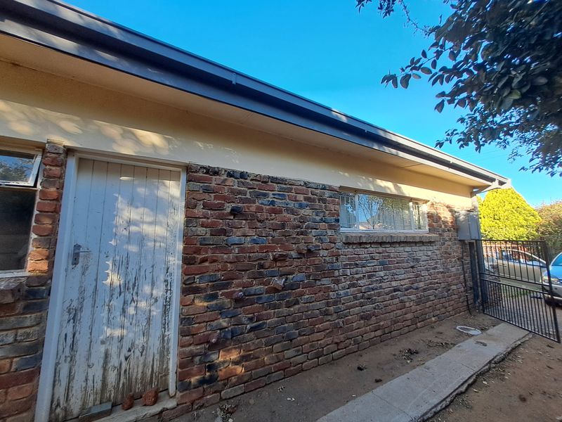 Rear exterior view of the property featuring exposed brickwork, a metal security gate, and a weathered door.