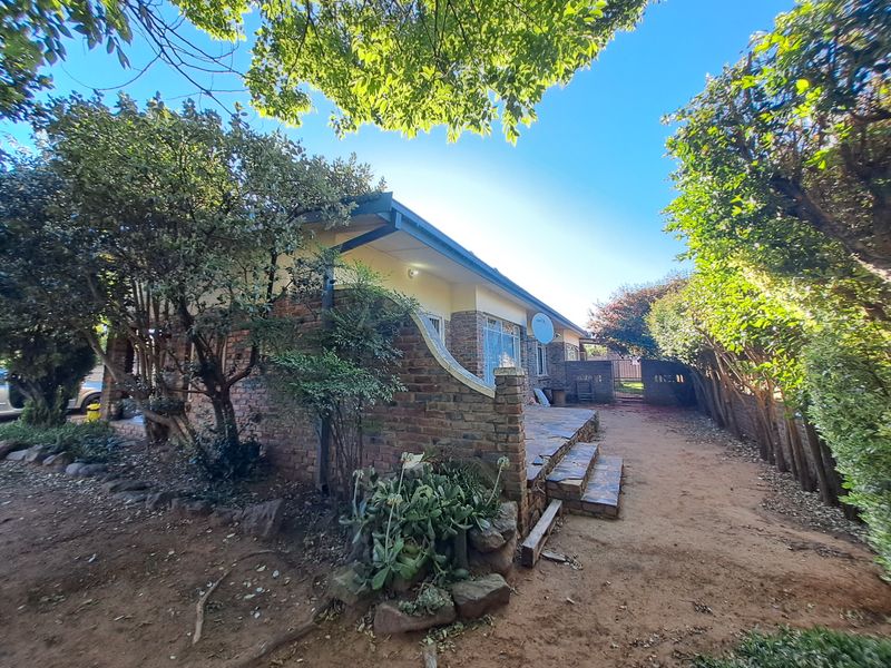Rear view of the house featuring a brick facade, a tiled patio area, and established garden surroundings.