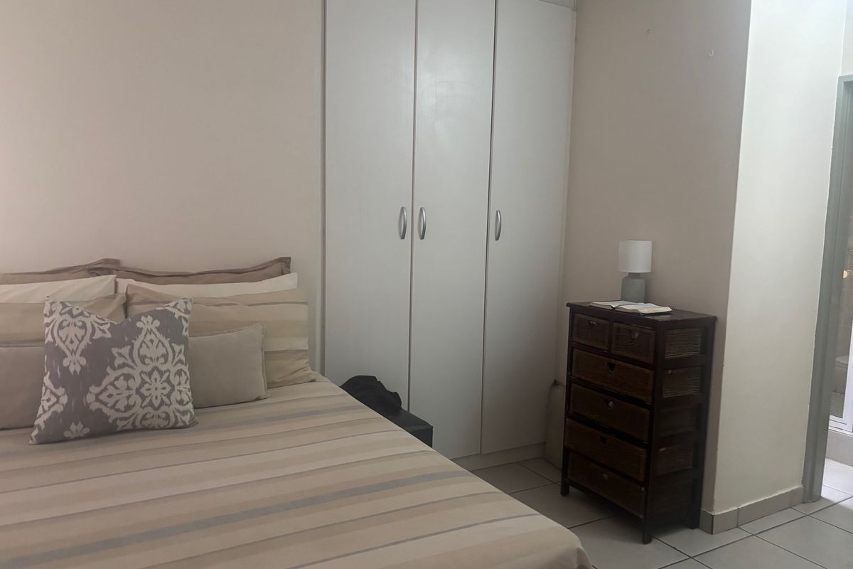 A bedroom featuring neutral tiled flooring and a white built-in wardrobe with ample storage space.