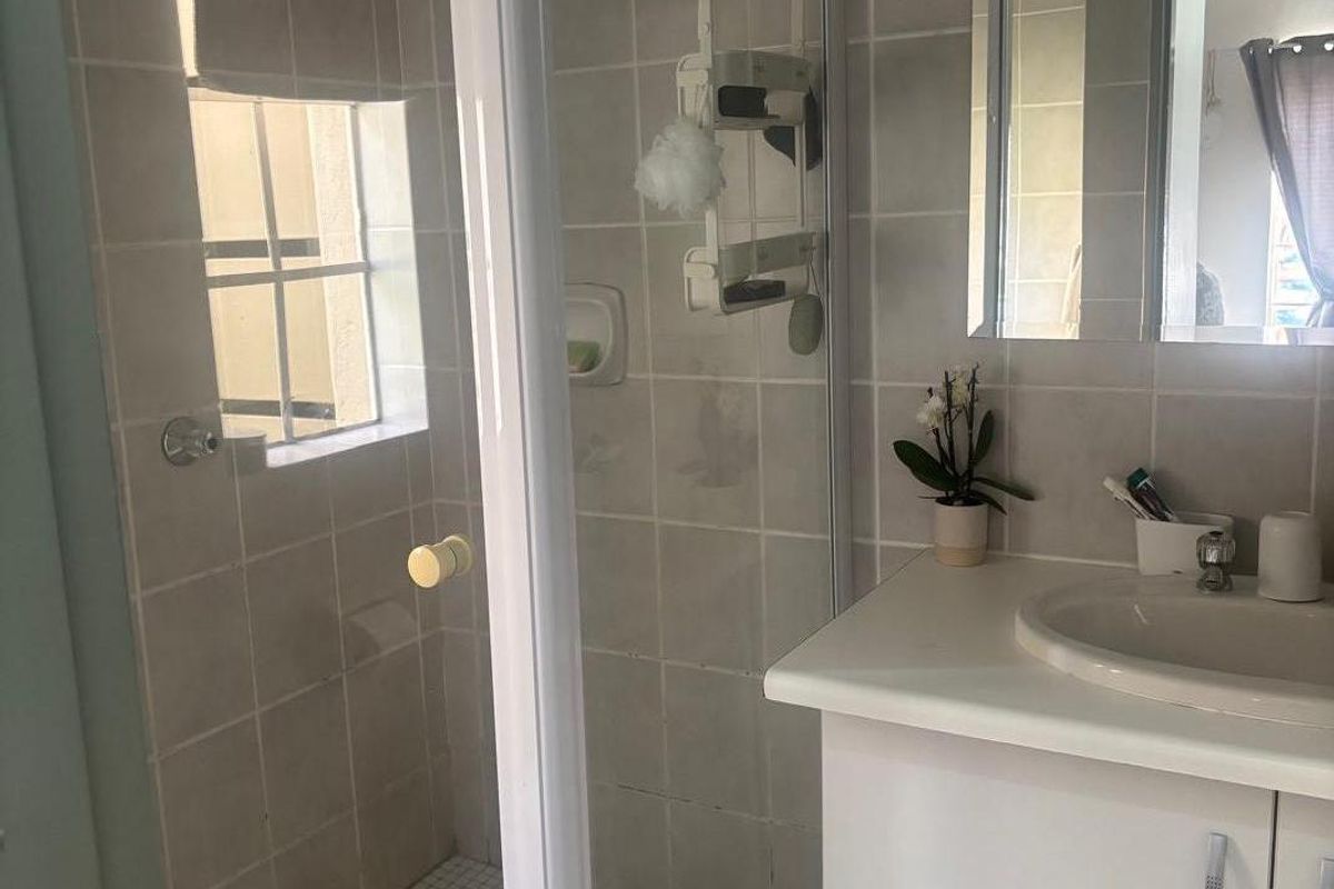 A functional bathroom featuring a shower enclosure, a vanity cabinet with an integrated sink, and neutral wall tiling.