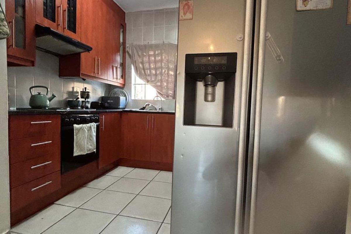 A functional kitchen featuring wooden cabinetry, tiled flooring, and built-in appliances, offering a practical layout with potential for modern updates.