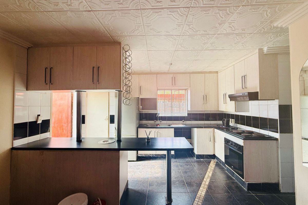 A functional kitchen featuring light-toned cabinetry, a breakfast bar, built-in oven, and hob, complemented by dark tiled flooring and a decorative ceiling.