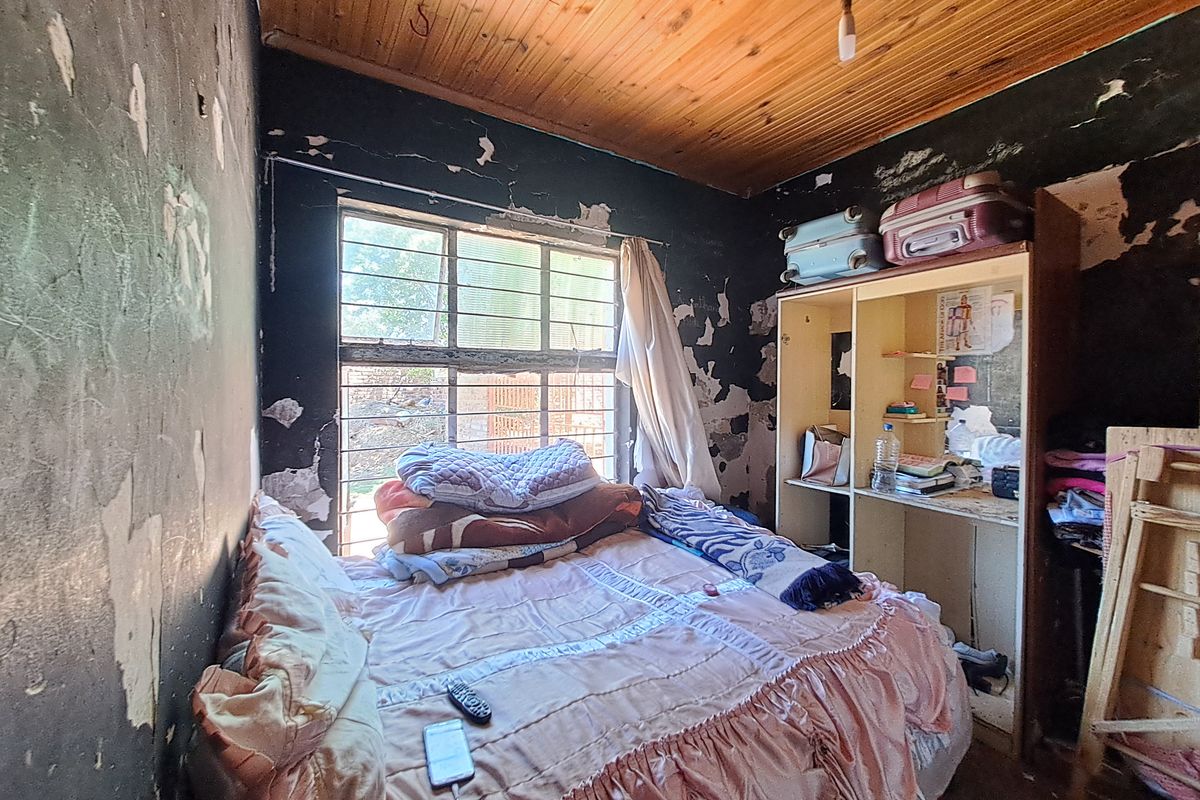 A bedroom featuring a timber ceiling and built-in wardrobe, currently requiring significant wall repairs and cosmetic renovation to restore the space.