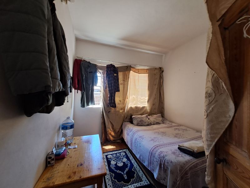 A compact bedroom featuring a window with curtains and a wooden door, providing a functional sleeping space.