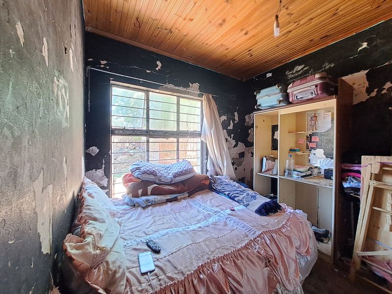 A bedroom featuring a timber ceiling and steel window frame, currently requiring significant wall repairs and cosmetic renovation to restore its condition.