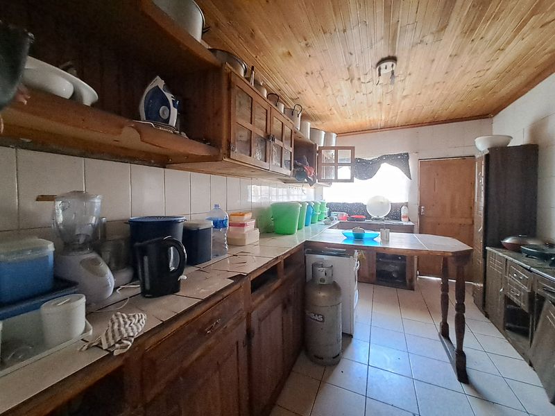 A dated kitchen featuring wooden cabinetry, tiled countertops, and a timber ceiling, offering significant potential for modernization and renovation.