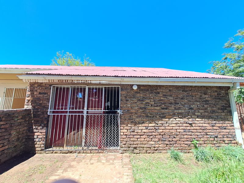 Rear exterior view of the house featuring a face brick facade, corrugated metal roof, and a secured sliding door entrance.