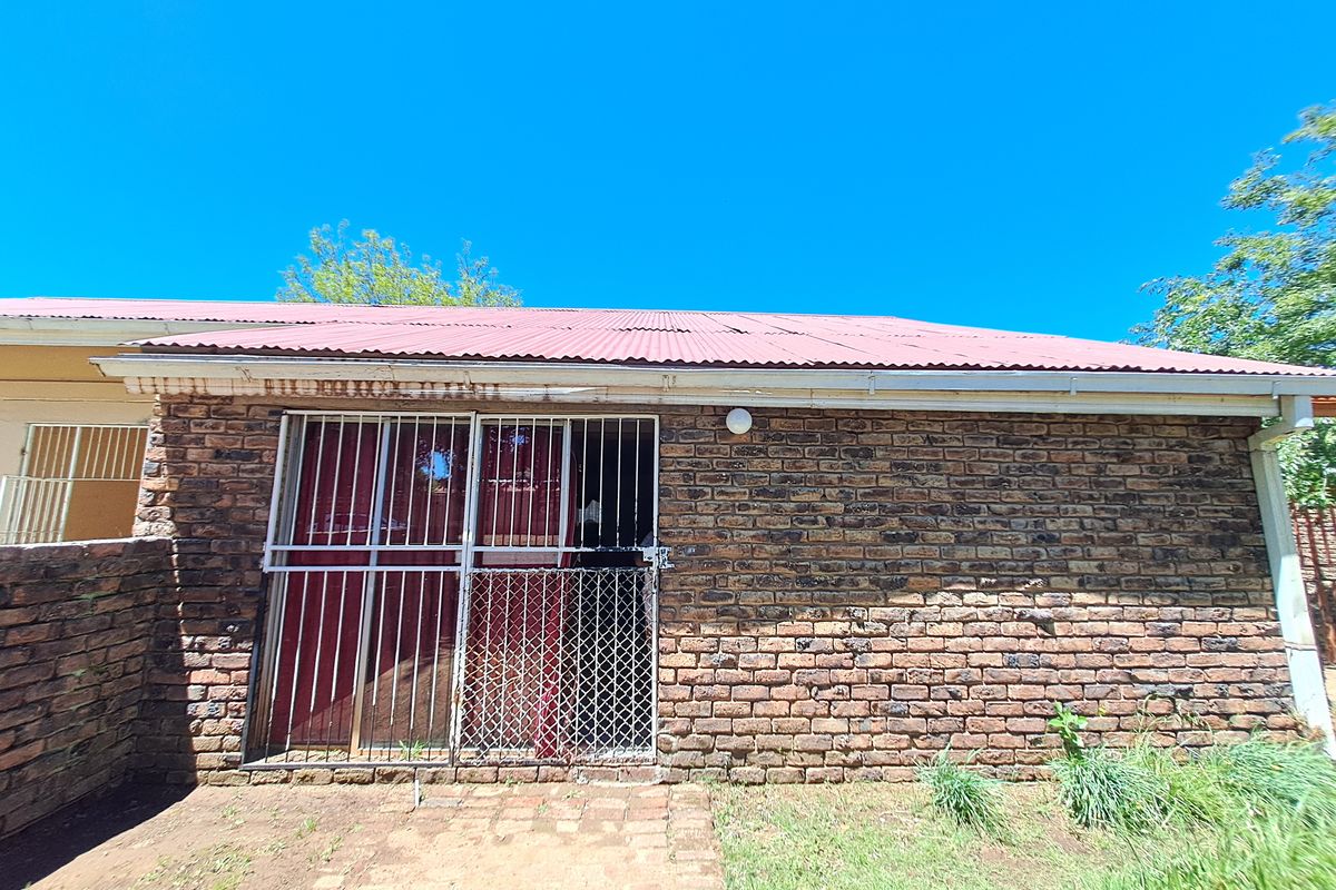 Rear exterior view of the house featuring a face brick facade, corrugated metal roof, and a secured sliding door entrance.