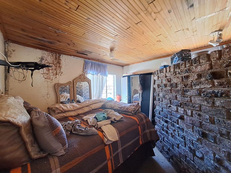 Bedroom featuring a rustic exposed brick wall and timber ceiling, currently requiring significant wall repairs and cosmetic refurbishment.