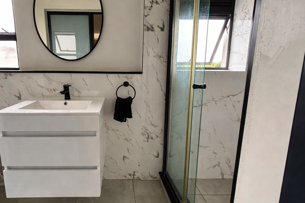 Modern bathroom featuring a floating vanity, marble-look wall tiles, and a sleek glass shower enclosure with contemporary black fixtures.