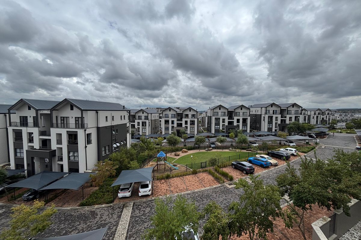 Aerial view of a modern townhouse complex featuring paved driveways, covered parking, and a central communal garden with a playground.