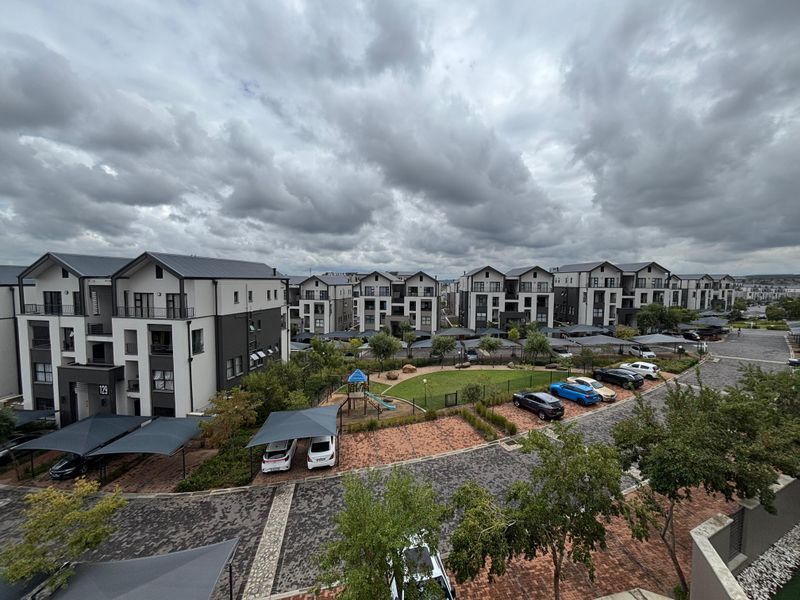 Aerial view of a modern townhouse complex featuring paved driveways, covered parking, and a central communal garden with a playground.