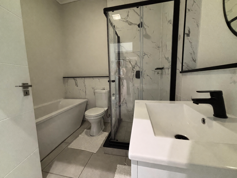 Modern bathroom featuring a freestanding bathtub, glass shower enclosure, vanity basin with black matte fixtures, and elegant marble-look wall tiling.
