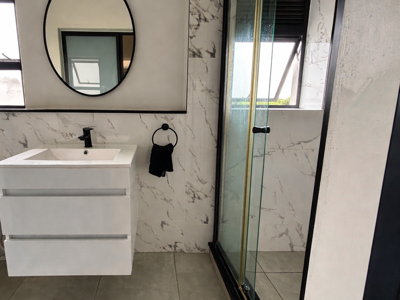 Modern bathroom featuring a floating vanity, marble-look wall tiles, and a sleek glass shower enclosure with contemporary black fixtures.
