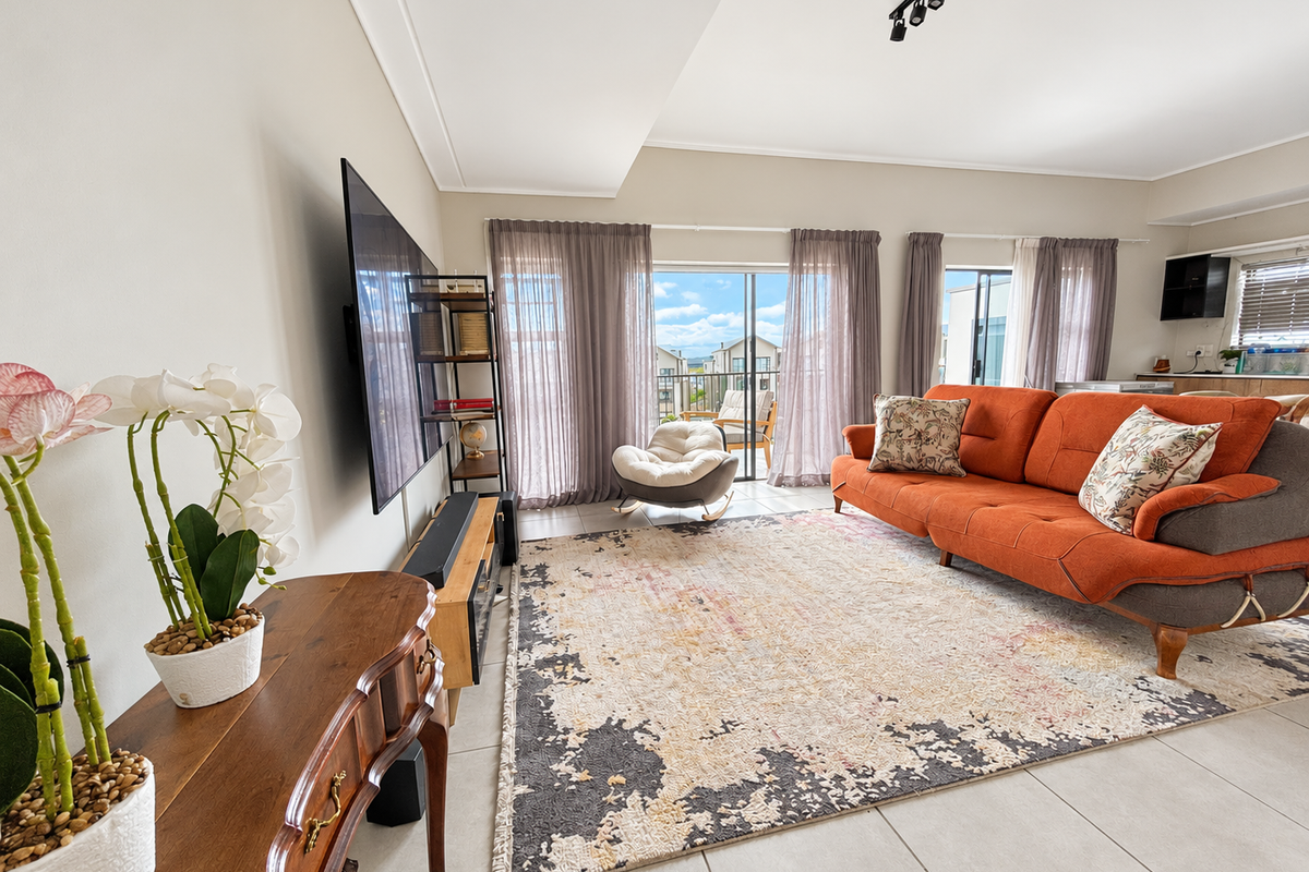 A bright and spacious living room featuring large sliding glass doors that open to a balcony, complemented by modern track lighting and tiled floors.