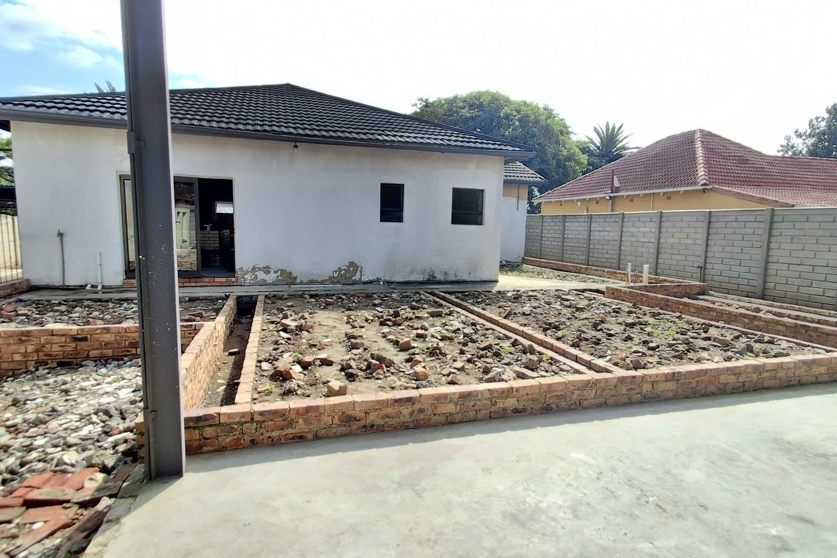 Rear exterior view of the property featuring a concrete patio, unfinished brick garden beds, and a perimeter boundary wall.