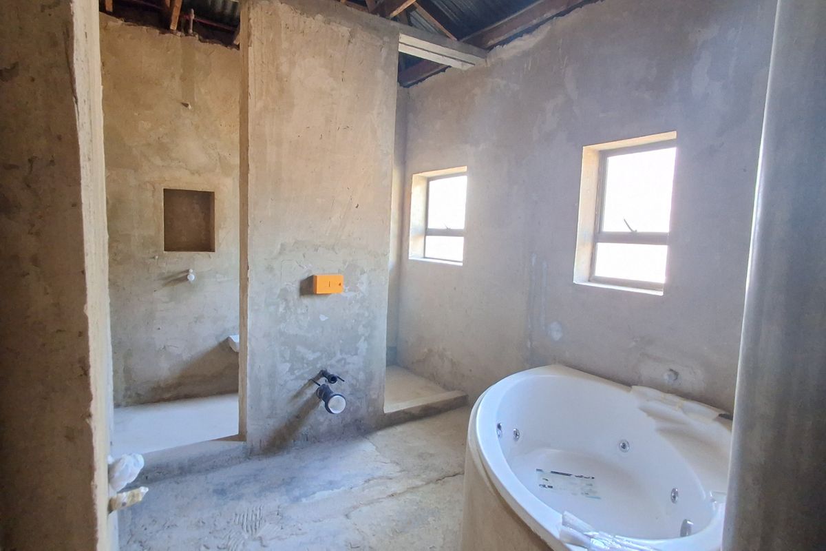 An unfinished bathroom space in shell condition, featuring a built-in bathtub, plumbing rough-ins, and exposed concrete walls awaiting final finishes.