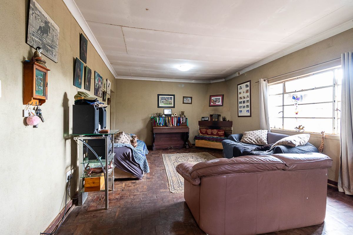 A spacious living room featuring original parquet flooring, large windows for natural light, and a coved ceiling, offering potential for modernization.