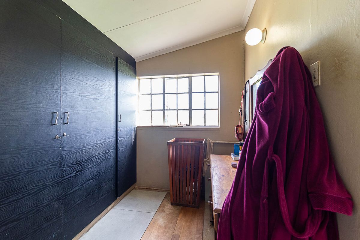 A bedroom featuring dark built-in cupboards, a steel-framed window, and a sloped ceiling, offering a functional space with potential for cosmetic updates.