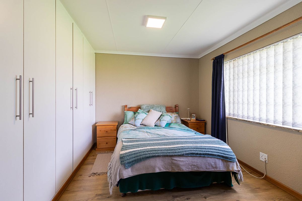 A well-maintained bedroom featuring neutral walls, laminate flooring, and extensive built-in cupboard storage with modern handles.