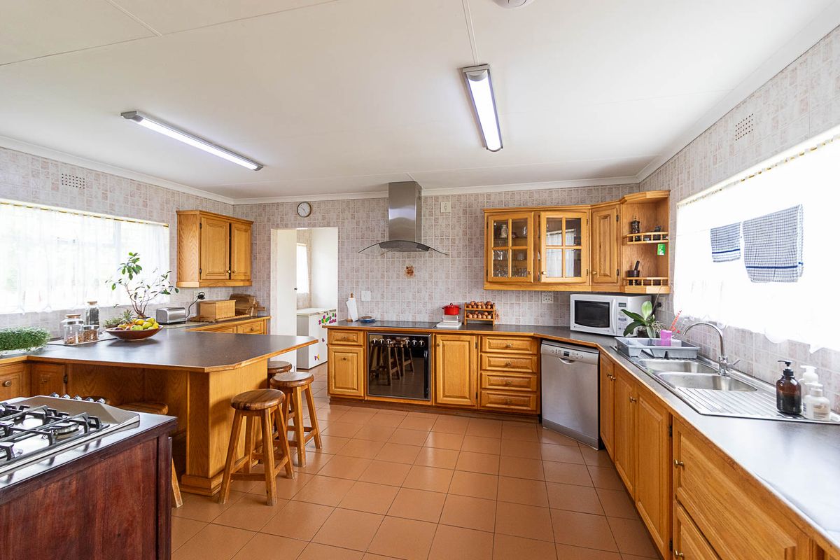 Spacious kitchen featuring wooden cabinetry, laminate countertops, a built-in oven with gas hob, stainless steel extractor fan, and tiled flooring.