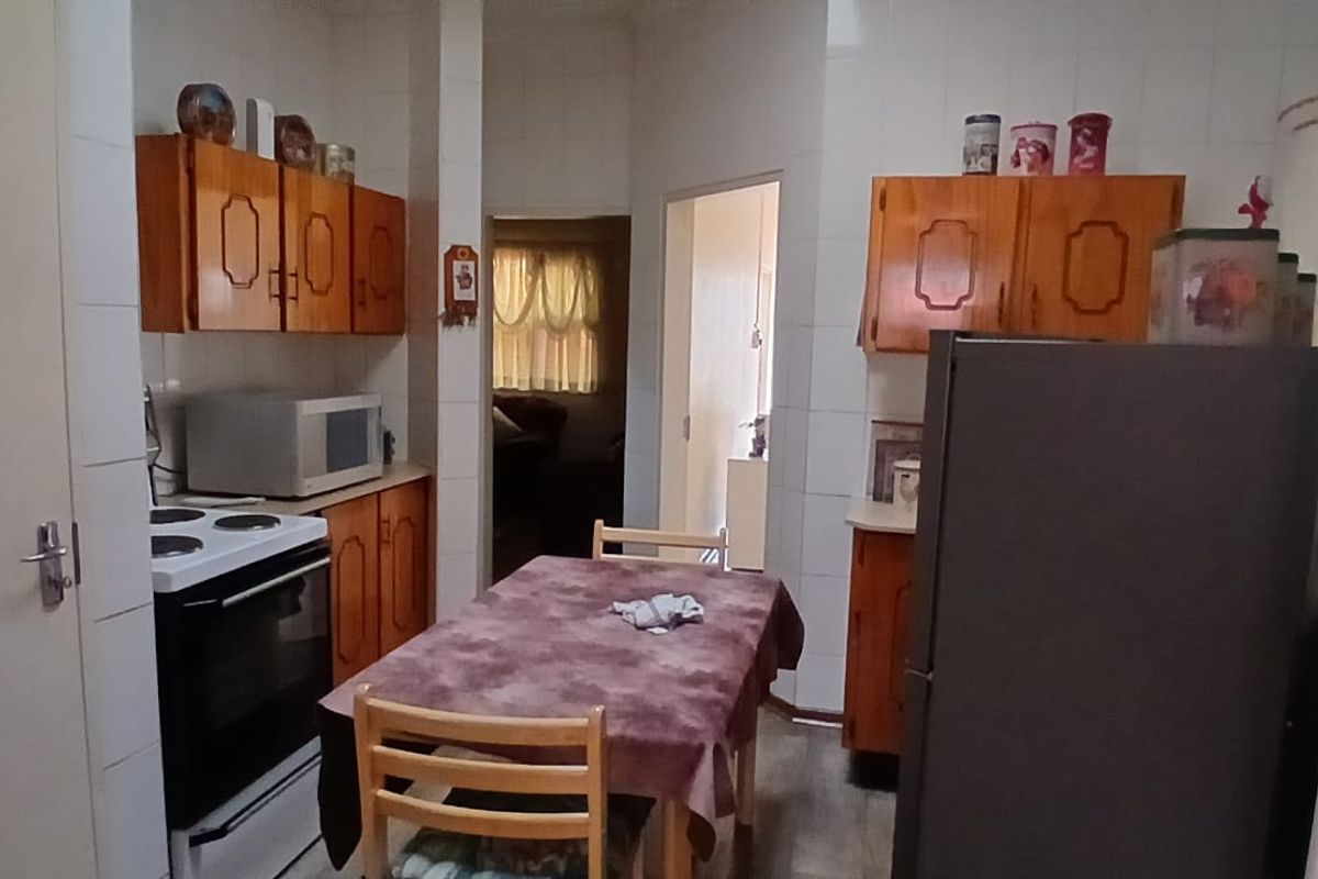 A compact kitchen featuring wooden cabinetry, tiled walls, and a freestanding stove, providing a functional layout with direct access to adjacent living areas.