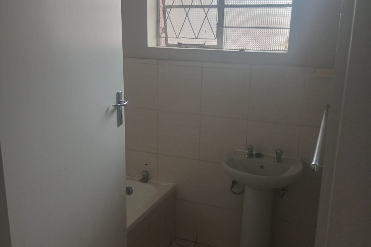 A functional bathroom featuring a pedestal basin, bathtub, and tiled finishes, requiring some cosmetic updates to modernize the space.